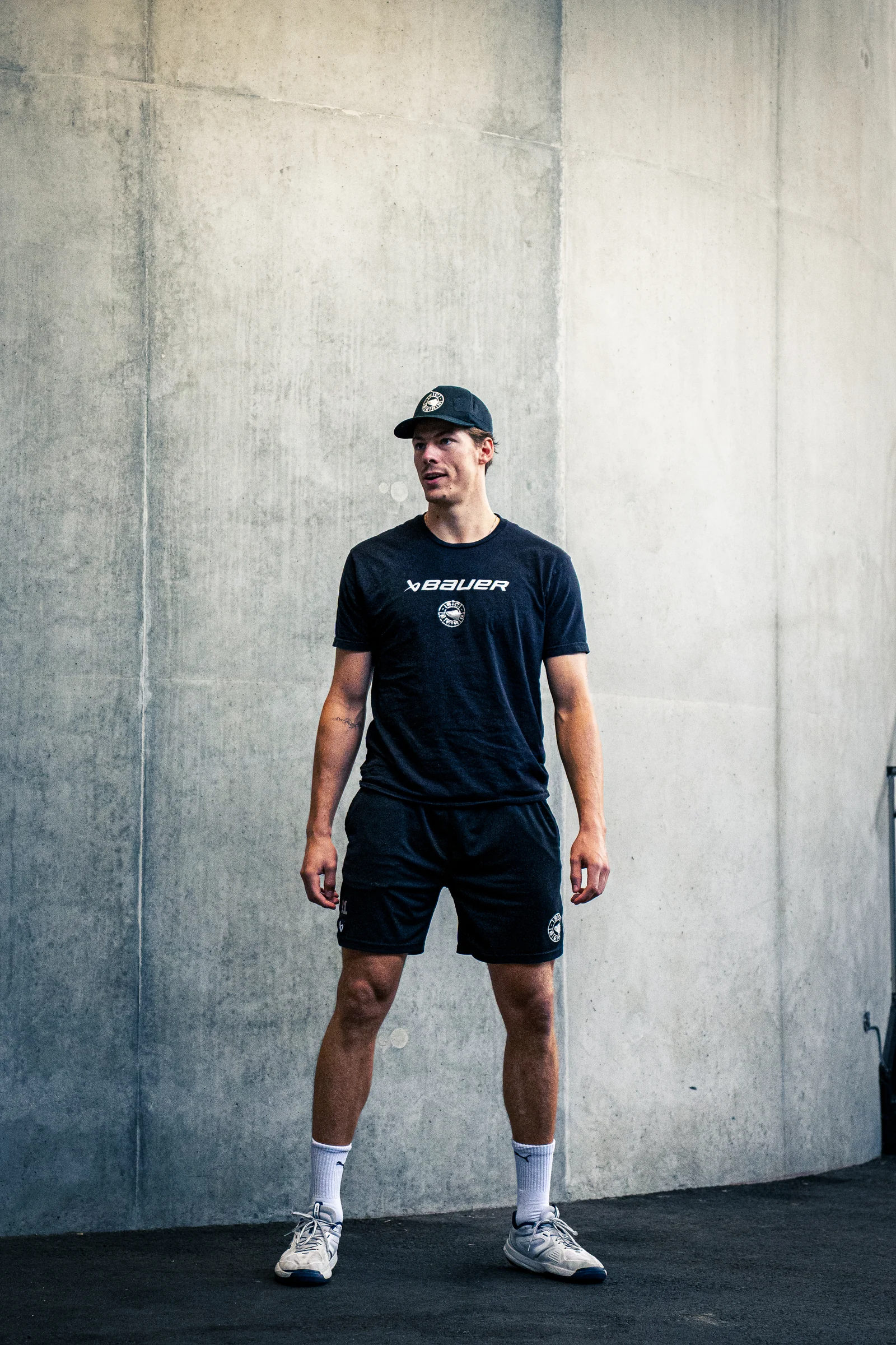 Mann in schwarzer Sportkleidung und Kappe vor einer Betonwand