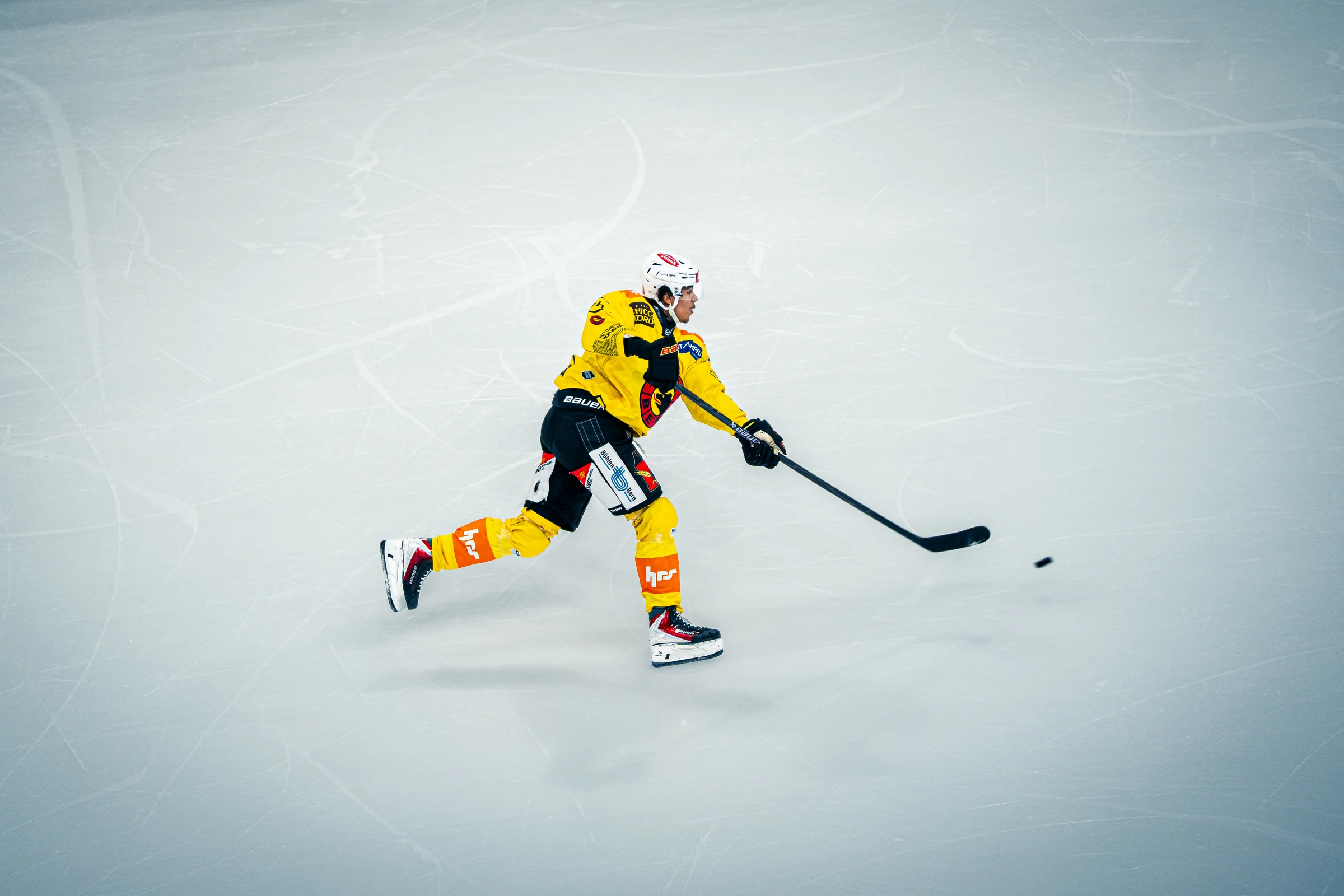 Eishockeyspieler in Gelb mit Schläger und Puck auf dem weiten Eisfeld