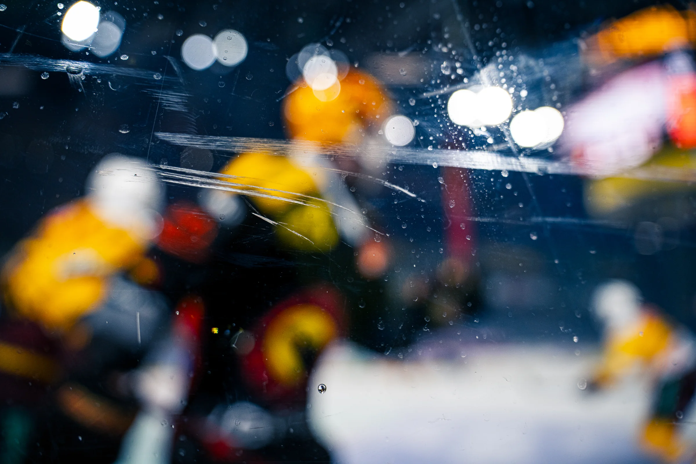 Eishockeyspieler und Hallenlichter unscharf hinter Wassertropfen auf der Scheibe